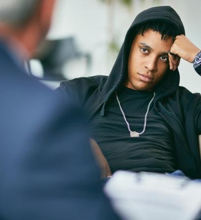 Black male adolescent listening to his counsellor during therapy session at psychotherapist's.