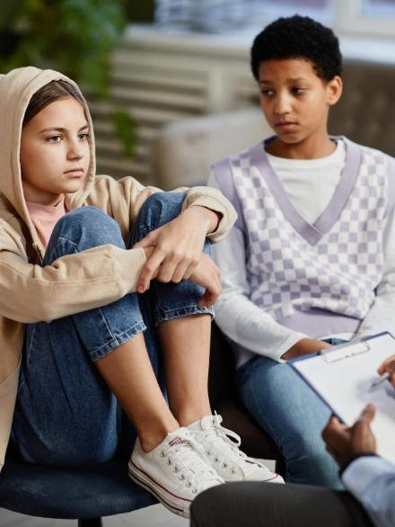 Portrait of teenage girl wearing hoodie in group therapy session with diverse children